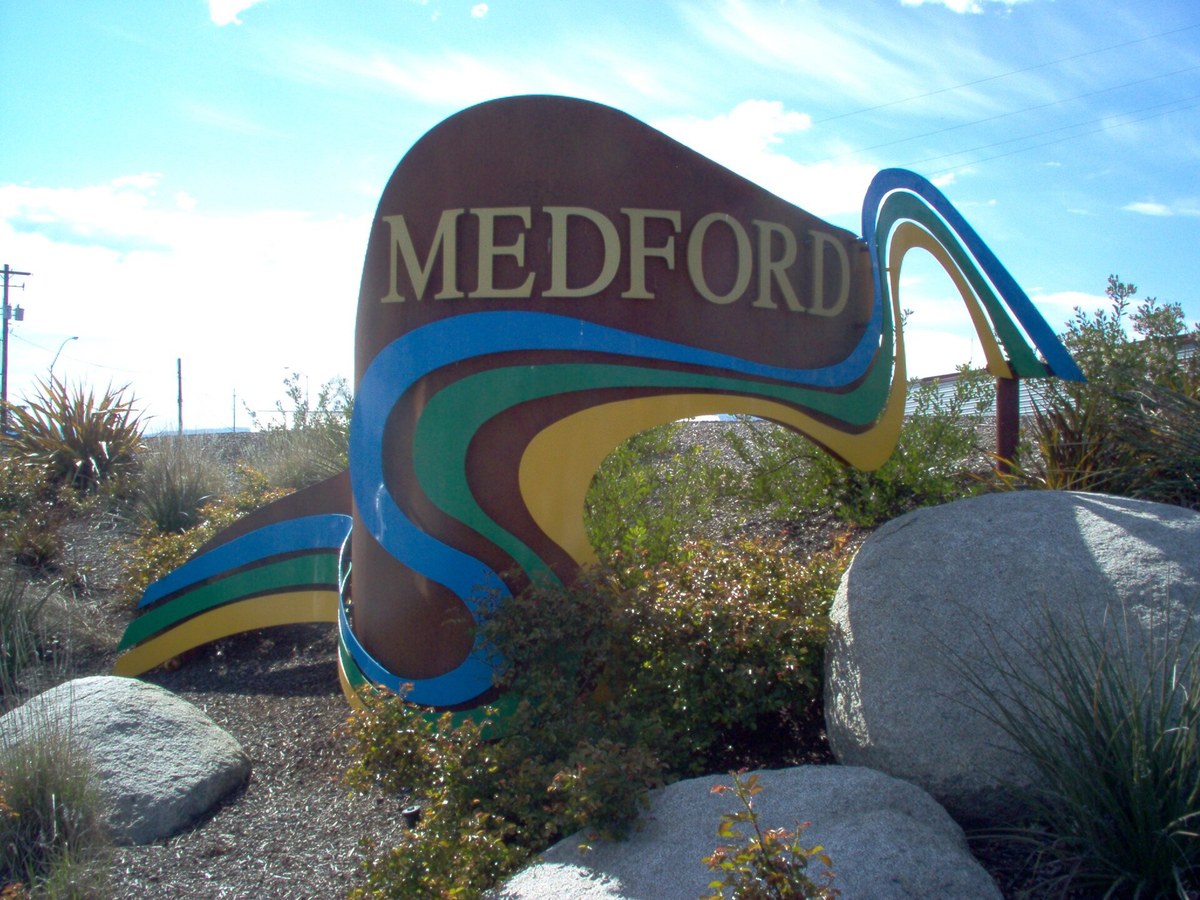 The Medford city welcome sign, a curved bronze-colored sculpture with blue, green and gold ribbons